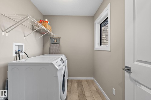 Dedicated laundry room featuring wood-finish flooring, a white paneled door with brushed nickel hardware, and a window providing natural light - 2146 Koshal Way, Edmonton, AB 