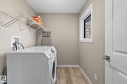 Dedicated laundry room featuring wood-finish flooring, a white paneled door with brushed nickel hardware, and a window providing natural light - 
