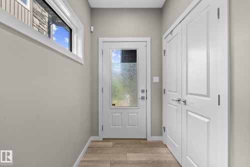 Entryway featuring a white paneled door with frosted glass, wood-finish flooring, a transom window, and a double-door storage closet with brushed nickel hardware - 2146 Koshal Way, Edmonton, AB 