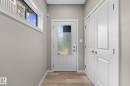 Entryway featuring a white paneled door with frosted glass, wood-finish flooring, a transom window, and a double-door storage closet with brushed nickel hardware - 2146 Koshal Way, Edmonton, AB 