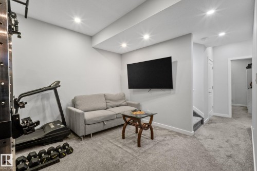Carpeted recreation area featuring recessed lighting, a wall-mounted television, and a staircase leading to an upper level - 2146 Koshal Way, Edmonton, AB 