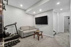 Carpeted recreation area featuring recessed lighting, a wall-mounted television, and a staircase leading to an upper level - 