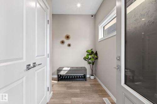 Entryway featuring light wood-finish flooring, a contemporary overhead light fixture, white trim, and a horizontal window providing natural illumination - 2146 Koshal Way, Edmonton, AB 