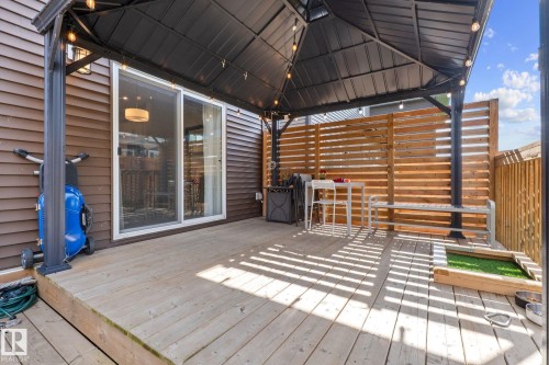Outdoor wooden deck featuring a metal gazebo with string lights, brown horizontal siding, a sliding glass door, and a wooden privacy screen - 2146 Koshal Way, Edmonton, AB 