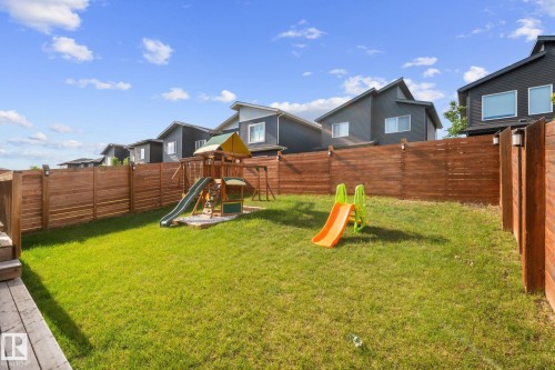 Expansive backyard featuring a green lawn, wood privacy fencing, and exterior lighting fixtures - 2146 Koshal Way, Edmonton, AB 