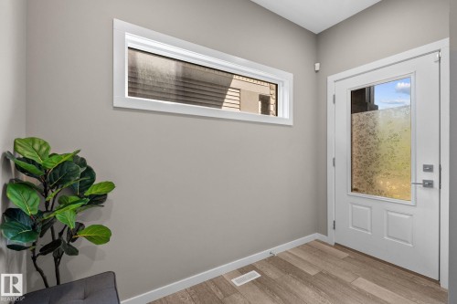Entryway featuring a white paneled door with a frosted glass insert, wood-finish flooring, and a horizontal transom window - 2146 Koshal Way, Edmonton, AB 