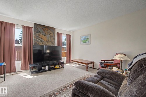 Living area featuring a stone accent wall, light-colored carpeting, and multiple windows with privacy coverings - 18409 66 Avenue, Edmonton, AB 