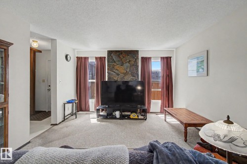 Living area featuring a stone accent wall, light gray carpeting, and white painted walls - 18409 66 Avenue, Edmonton, AB 