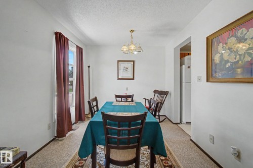 Dining area featuring a single window with curtain rod, patterned carpeting, and a ceiling-mounted chandelier - 18409 66 Avenue, Edmonton, AB 