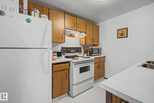 Kitchen featuring wood-finish cabinetry, white countertops, and a double basin stainless steel sink - 18409 66 Avenue, Edmonton, AB 