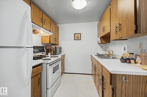 Galley kitchen featuring wood-finish cabinetry, white countertops, and white appliances - 18409 66 Avenue, Edmonton, AB 