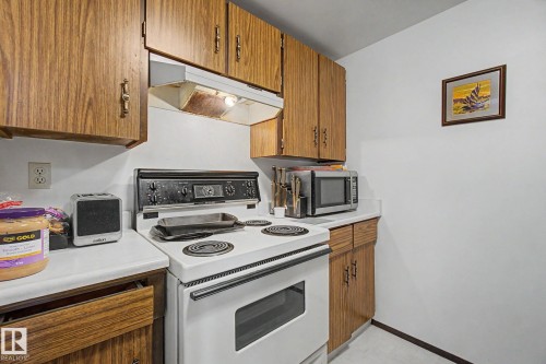 Kitchen area featuring wood-finish cabinetry, white countertops, a white electric range, and a built-in range hood - 18409 66 Avenue, Edmonton, AB 