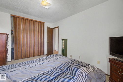 Room featuring wood-finish accordion closet doors, white walls, textured ceiling, and a flush-mount ceiling light fixture - 18409 66 Avenue, Edmonton, AB 