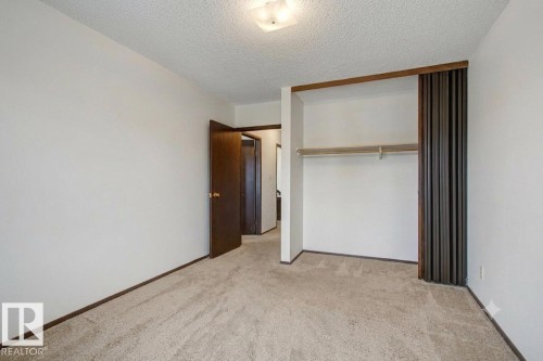 Carpeted room featuring a built-in closet with sliding dark wood doors and an integrated clothing rod - 18409 66 Avenue, Edmonton, AB 