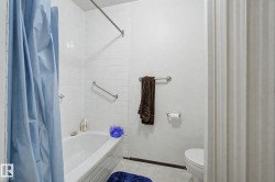 Bathtub with white subway tile surround, chrome grab bars, and a chrome shower rod - 