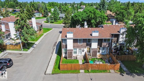 Townhome complex featuring brown siding and white accents, individual fenced yard spaces, and dedicated parking - 18409 66 Avenue, Edmonton, AB 