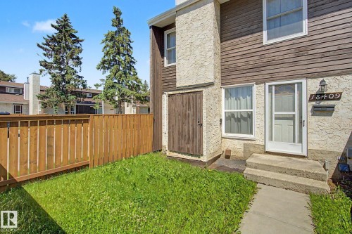 Exterior featuring a private grassed yard, wood privacy fence, and concrete entry steps - 18409 66 Avenue, Edmonton, AB 
