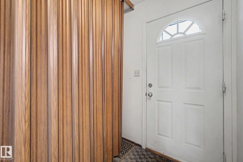 Entryway featuring a white panel door with an arched transom window, wood-finish slatted wall paneling, and checkered flooring - 18409 66 Avenue, Edmonton, AB 