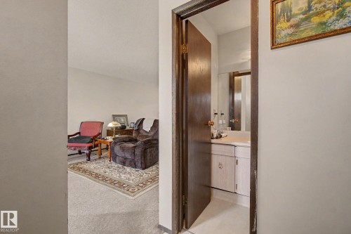 Well-lit interior hallway with a wood-trimmed doorway opening to a bathroom featuring a vanity with a countertop and built-in cabinetry - 18409 66 Avenue, Edmonton, AB 