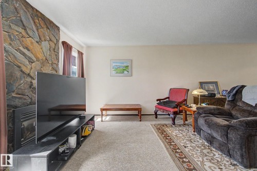 Living room featuring a stone-clad fireplace surround, neutral wall paint, and light-toned carpet flooring - 18409 66 Avenue, Edmonton, AB 