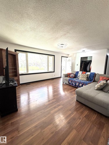 Spacious living area featuring polished wood-finish flooring, a prominent picture window with black trim, and a contemporary flush-mount ceiling light fixture - 45 Lambert Crescent, St. Albert, AB 
