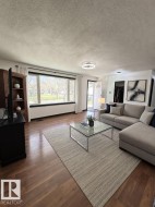 Light-filled living space featuring wood-finish flooring, a large picture window with black trim, and a contemporary ceiling light fixture - 