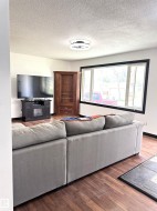 Living area featuring wood-finish flooring, a large multi-pane window with dark trim, a ceiling-mounted light fixture, and white wall paint - 