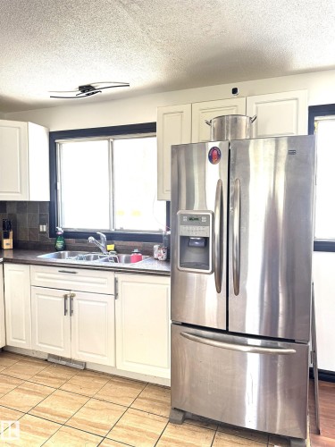Kitchen featuring a stainless steel French door refrigerator, white cabinetry, a dual basin stainless steel sink, and a tiled backsplash - 45 Lambert Crescent, St. Albert, AB 