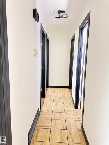 Hallway featuring light-toned square tile flooring, white walls, dark trim, and multiple doorways - 45 Lambert Crescent, St. Albert, AB 
