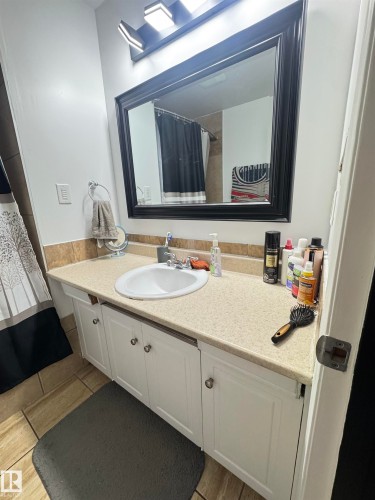 Bathroom vanity with an integrated sink, light-colored countertop, and a framed mirror illuminated by a modern light fixture - 45 Lambert Crescent, St. Albert, AB 