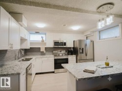 Kitchen featuring white cabinetry, light-toned countertops, stainless steel appliances, a tiled backsplash, and recessed and pendant lighting - 