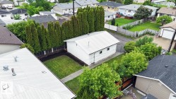 Detached outbuilding with white siding and a metal roof, situated on a grassy lot - 