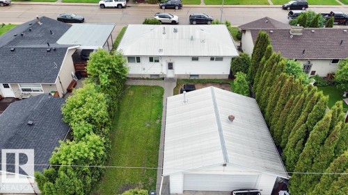 Rear yard featuring a detached garage with a white garage door, a manicured lawn, and mature privacy trees - 7515 130 Avenue, Edmonton, AB 