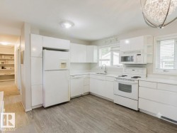 Kitchen featuring wood-finish flooring, white cabinetry, white countertops, and white appliances including a refrigerator, dishwasher, and range with microwave above - 