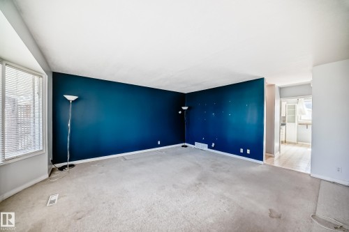 Living area featuring a prominent accent wall, bay window, and light-toned carpeting - 7317 83 Avenue, Edmonton, AB 