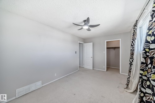 Carpeted room featuring a ceiling fan with integrated lighting, a white painted door, and an open closet with a clothing rod - 7317 83 Avenue, Edmonton, AB 