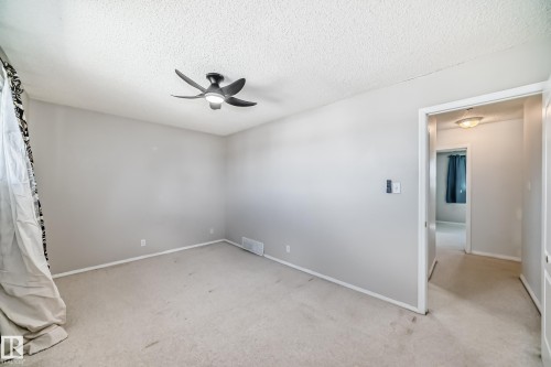 Spacious room featuring neutral carpeting, light gray wall paint, and a ceiling fan with integrated lighting - 7317 83 Avenue, Edmonton, AB 
