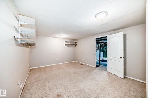 Carpeted room featuring neutral-toned walls, ceiling-mounted lighting fixtures, and a white interior door with brass hardware - 7317 83 Avenue, Edmonton, AB 