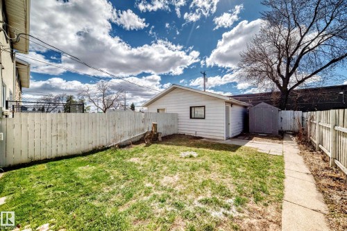 Rear exterior featuring a detached garage (single), a storage shed, a concrete pathway, and a white picket fence enclosing the yard - 7317 83 Avenue, Edmonton, AB 