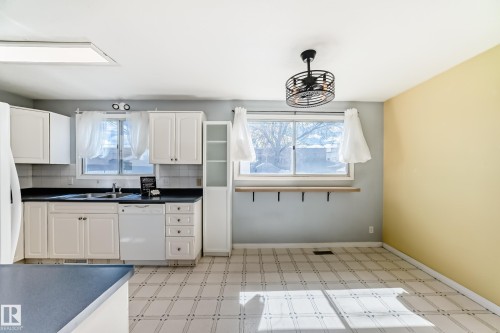 Kitchen area featuring white cabinetry, dark countertops, and a white tile backsplash - 7317 83 Avenue, Edmonton, AB 