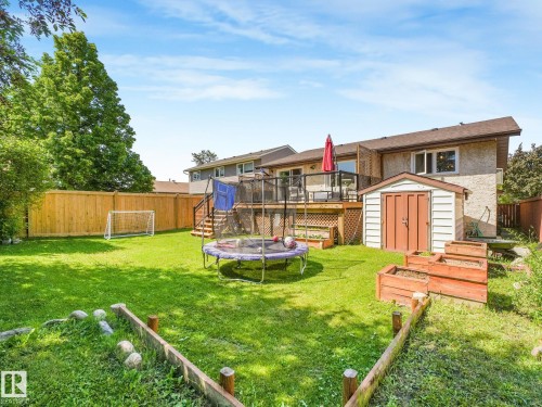 Spacious rear yard featuring an expansive lawn, tiered wood deck with glass railing, and a storage shed - 2035 49A Street, Edmonton, AB 