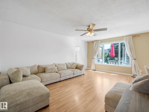 Bright living space featuring expansive windows, light wood-finish flooring, a ceiling fan with integrated lighting, and neutral wall tones - 2035 49A Street, Edmonton, AB 