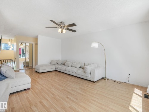 Spacious living area featuring light wood-finish flooring, white walls, and a ceiling fan with integrated lighting - 2035 49A Street, Edmonton, AB 