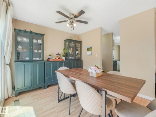 Light-toned wood-finish flooring provides a bright foundation for this dining area, featuring a dark wood-tone table and a ceiling fan with integrated lighting - 2035 49A Street, Edmonton, AB 