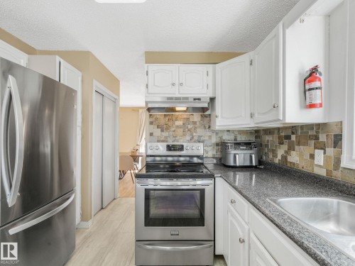 Kitchen featuring stainless steel appliances, white cabinetry, a stone tile backsplash, dark speckled countertops, and a double basin sink - 2035 49A Street, Edmonton, AB 