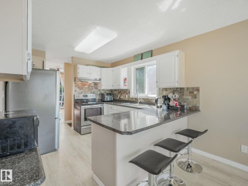 Kitchen featuring white cabinetry, dark stone countertops, stainless steel appliances, a tiled backsplash, and wood-finish flooring - 2035 49A Street, Edmonton, AB 