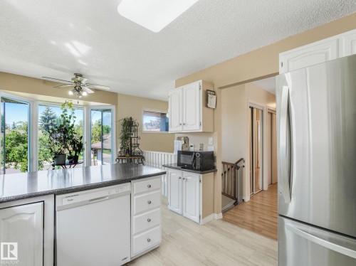 Kitchen featuring an island with a built-in dishwasher, white cabinetry, dark countertops, and a stainless steel refrigerator - 2035 49A Street, Edmonton, AB 