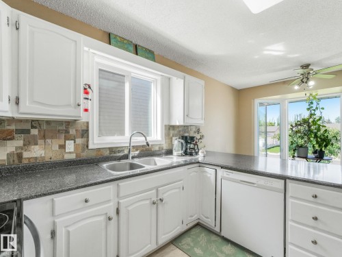 Kitchen featuring white cabinetry, a double basin stainless steel sink, dark speckled countertops, and a mosaic tile backsplash - 2035 49A Street, Edmonton, AB 