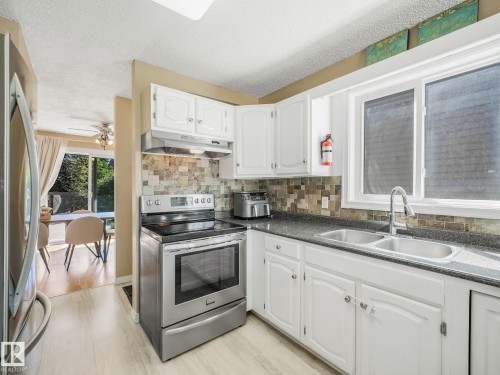 Kitchen featuring white cabinetry, stainless steel appliances, a mosaic tile backsplash, and dark countertops - 2035 49A Street, Edmonton, AB 