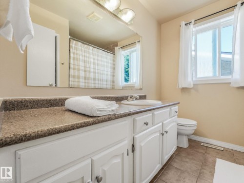 Bathroom vanity featuring white cabinetry, a speckled countertop, an integrated sink, and brushed nickel hardware - 2035 49A Street, Edmonton, AB 